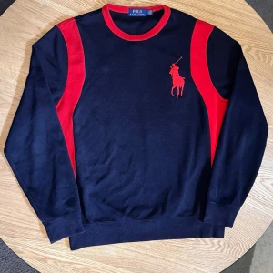 Polo Ralph Lauren Sweatshirt Navy/Röd – Stort ryggtryck - Säljer en riktigt fet Polo Ralph Lauren sweatshirt i navy med röda detaljer.  Stort rött polo-tryck på bröstet + stort emblematiskt ryggtryck (Polo Ralph Lauren Est. 1967). Röda paneler på ärmarna och röd kant i halsen.  Skick: Mycket bra. Tvättad och klar. Inga synliga defekter.  En av de snyggare modellerna – både fram- och baksida har stark look.  Storlek: M Mått kan tas vid förfrågan.
