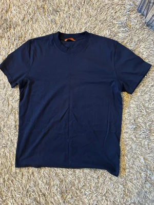 Mörkblå t-shirt med gul detalj Pjs - Snygg mörkblå t-shirt med gul söm längs axeln och ett litet broderat märke på ärmen. Klassisk rund halsringning och korta ärmar. Perfekt för en clean och stilren look. Märkt PJS på ärmen. Använd 1 gång