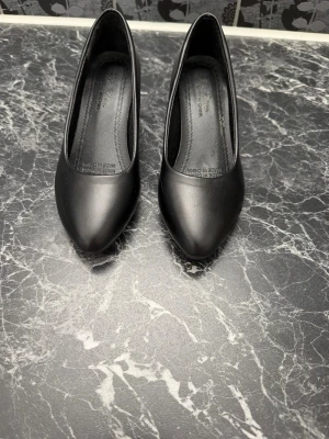 Svarta klassiska pumps med låg klack - Stilrena svarta pumps med spetsig tå och låg klack. Skorna är tillverkade i ett slätt, matt material som ger en elegant look. 