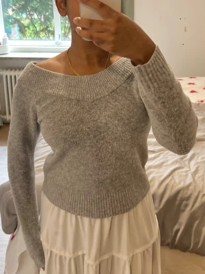 Grå stickad tröja från HM - Mysig grå stickad tröja med bred ribbad off shoulder-ringning och långa ärmar från hm i storlek xs. Passar även för personer i storlek S. Tröjan har en mjuk och fluffig känsla, perfekt för kyliga dagar. Passar snyggt till både kjol och jeans för en avslappnad look. Lite nopping med i övrigt bra skick. 