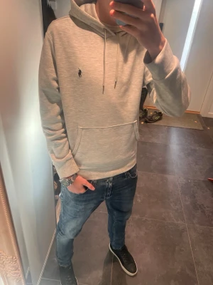Ralph Lauren hoodie  - Säljer en stilren ljusgrå hoodie med huva och dragsnören. Hoodien har en broderad logga på bröstet och en stor magficka framtill. Tillverkad i mjukt material som känns skönt mot huden. Perfekt för dig som gillar en clean och avslappnad look.