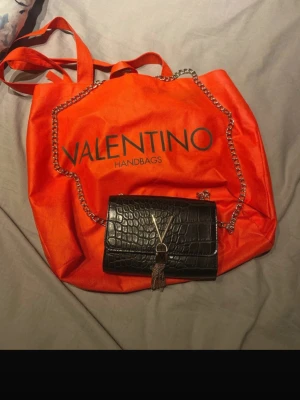 Valentino väska  - Säljer denna jättesnygga Valentino axelväska! Använd ett få gånger men kommer i mycket bra skick! Har inga skador osv! Färgen på själva märket på väskan (även de små kedjorna) har rostat pyte lite men det syns inte!!!! Så inget man tänker på! Man får även med den orange påsen med! Priset går inte att diskuteras på denna eftersom den är köpt för 1200kr och har inga skador! 