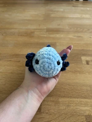 Virkad axelot - Supergullig handvirkad axelot i ljusblått garn med mörkblå detaljer och svarta säkerhetsögon. Perfekt som prydnad eller mysig liten maskot. Tillverkad i mjukt, fluffigt garn och får plats i handen.