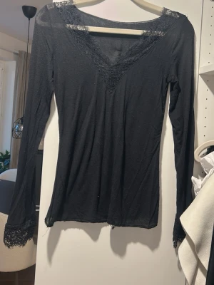 Svart långärmad Intimissimi tröja med spets - Svart långärmad topp med v-ringning och spetsdetaljer vid halsringning och ärmslut. Tunn och mjuk, perfekt att styla lager på lager eller som den är. Snygg och enkel att matcha till olika outfits.