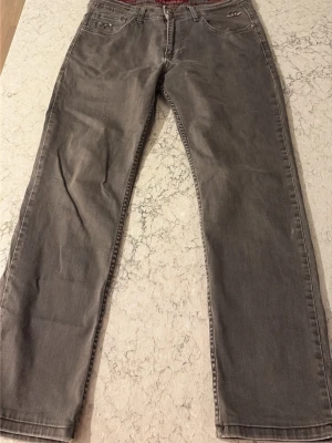 Grå raka jeans med broderade fickor - Snygga grå jeans med rak passform och broderade detaljer på bakfickorna. Klassisk femficksmodell och normal midja. Perfekta till en avslappnad stil och passar till det mesta. Tillverkade i mjukt denimtyg för skön känsla.