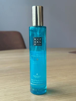 Rituals The Ritual of Karma mist - Fräsch hår- och kroppsmist från Rituals i serien The Ritual of Karma. Flaskan är turkosblå med guldfärgat lock och rymmer 50 ml. Doften har inslag av helig lotus och vit te, och flaskan är tillverkad i plast med elegant design.