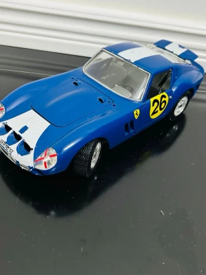 Blå modellbil Ferrari 250 GTO - Säljer en detaljerad modellbil av en Ferrari 250 GTO i blått med vita racingränder och nummer 26 på sidorna. Bilen har silverfärgade fälgar, realistiska detaljer och genomskinliga fönster. Perfekt för dig som gillar bilar eller samlar på modellbilar.