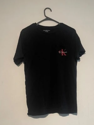 Calvin Klein jeans T-shirt - Snygg t-shirt från Calvin Klein Jeans med den klassiska CK-loggan tryckt i rött över bröstet. Tröjan är tillverkad i en mjuk och skön 100% bomullskvalitet som ger en riktigt skön passform. Det är ett perfekt och tidlöst basplagg som fungerar lika bra att bära som det är till ett par jeans eller att ha som ett lager under en hoodie eller jacka. Storlek L för barn 