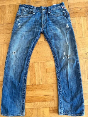 Blå retro Replay jeans vintage jeans med snygga slitningar. Storlek W34-L32. - Säljer ett par blå jeans med slitningar från Replay  och hål för en cool, avslappnad look. Jeansen har raka ben, klassisk femficksmodell och kontrastsömmar. Materialet är denim i bomull. Perfekta för dig som gillar en trendig och casual stil.                                                                                 Fraktar inom 24h🚚.                                             Det är bara att höra va dig vid frågor eller liknande😊