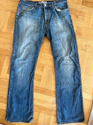 Blå raka J.Lindeberg jeans med snygga slitningar - Ett par riktigt feta blå J.Lindeberg jeans med raka ben och unika slitningar på låret och knät. Storlek: W34-L34. Bara att hör av dig vid frågor🙋‍♂️