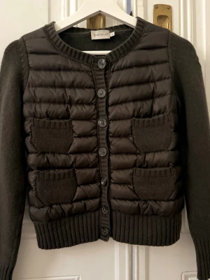 Jacka/kofta från Moncler (gamla modellen) - Superfin brun / svart Moncler jacka. Har inga stora skador förutom ett litet hål på baksidan som knappt syns, men är fortfarande i ett väldigt bra skick!! Har använt ett par gånger men har inte hittat användning av den. Det är därför jag väljer att sälja den. 🥰