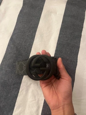 Svart bälte med GG-spänne - Snyggt svart bälte med stort GG-spänne i matt svart. Bältet har diskret mönster längs hela bandet och känns riktigt trendigt. Perfekt accessoar för att lyfta vilken outfit som helst. Man kan göra hål om man vill har gjort 2 hål 