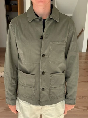 Olivgrön woolrich overshirt med fickor - Helt ny Olivgrön overshirt från woolrich i bomull med tre stora utanpåliggande fickor framtill och klassisk krage samt lapparna kvar. Stängs med fyra knappar och har raka ärmar. Enkel och clean design som passar till många stilar. Nypris 2800 kr