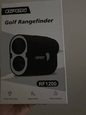 Golf avståndsmätare OPEN RF1200 - Golf Rangefinder RF1200 från OPEN i svart med vita detaljer. Avståndsmätaren har funktioner som kristallklar vy, slope switch och pulsvibration. Perfekt för att mäta avstånd på golfbanan. Kompakt och smidig design.