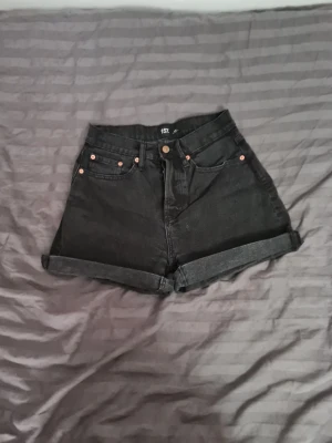 Svarta högmidjade jeansshorts - Snygga svarta jeansshorts från 157 med hög midja och uppvikta benslut. Klassisk femficksmodell med knappar framtill samt bälteshällor. Perfekta för en avslappnad och trendig look.