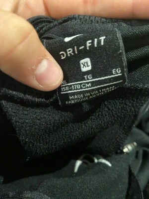 Svart Nike Dri-Fit långärmad tröja - Säljer en svart långärmad tröja från Nike med Dri-Fit-material som transporterar bort fukt. Perfekt för träning eller sportaktiviteter. Tröjan har en enkel och stilren design utan synliga tryck eller mönster.