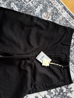 Svarta chinos från Axel Arigato - Helt nya, oanvända, med etiketter kvar. Storlek XS.                        Snygga svarta chinos från Axel Arigato med klassisk rak passform och bälteshällor. Byxorna har diskreta sidofickor och stängs med knapp och dragkedja. Tillverkade i ett mjukt och slitstarkt bomullstyg som ger en clean look.           Klassisk modell som passar till allt.  Hör av dig om du vill ha fler bilder eller fråga om mått
