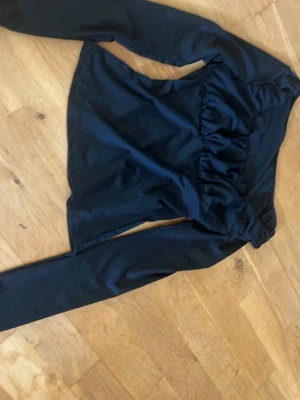 Svart långärmad topp från SHEIN - Snygg svart långärmad topp från SHEIN i glansig polyesterblandning. Toppen har en rynkad detalj framtill som ger en cool look och är perfekt att styla med jeans eller kjol. Materialet är mjukt och stretchigt för extra komfort.