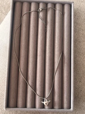 Halsband med hjärtlås och vingar - Snyggt silverfärgat halsband med ett hängsmycke i form av ett hjärta med lås och små vingar på sidorna. Kedjan är tunn och smidig med justerbar längd. Perfekt accessoar för dig som gillar unika detaljer och en touch av romantik.