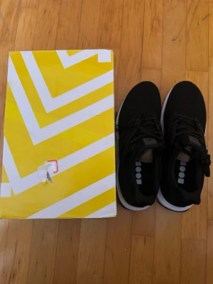 Adidas UltraBoost - Snygga svarta sneakers med stickad ovandel och vit sula. Skorna har klassisk snörning och en sportig look. Perfekta för dig som gillar stilrena och bekväma sneakers till vardags. Levereras med originalkartong.