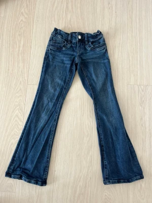 Mörkblå bootcut jeans  - Säljer ett par mörkblå bootcut jeans med klassisk femficksdesign och utsvängda ben. Jeansen har stretchig midja, knapp- och dragkedjestängning samt snygga slitningar framtill. Perfekta för dig som vill ha ett par bekväma jeans i stretchigt denimtyg.