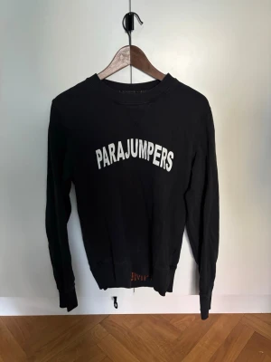 Svart fleece tröja Parajumpers - Svart långärmad fleece tröja från Parajumpers med vit logga tryckt över bröstet. Tröjan har rund halsringning och ribbade muddar vid ärmslut och nederkant. Perfekt för lager på lager och chill vardagsstil.