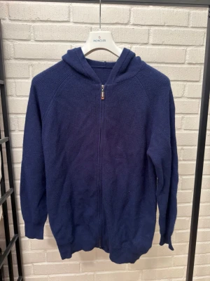 Mörkblå hoodie med dragkedja i kashmire blandning - En enkel och stilren mörkblå hoodie med dragkedja framtill och huva. Tillverkad i ett mjukt stickat material som känns skönt mot huden. Perfekt för en avslappnad look och funkar året runt. Långa ärmar och ribbade muddar ger en klassisk känsla.