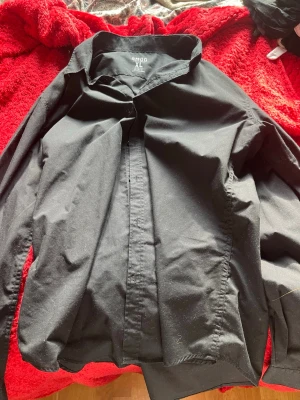 Svart skjorta med knappar - Klassisk svart skjorta i rak modell med långa ärmar och knappar framtill. Skjortan har en enkel och stilren design som passar till många olika looks. Tillverkad i ett mjukt och bekvämt material.