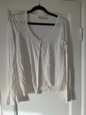 Vit ribbad kofta från Zara - Säljer en vit ribbad kofta från Zara med långa ärmar och rundad halsringning. Koftan har knappar framtill och är tillverkad i ett mjukt, tunt material som passar perfekt till lager på lager. Enkel och stilren design som funkar till det mesta.