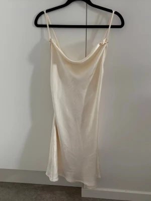 Satinklänning i champagne/cream  - Superfin satinklänning i en elegant champagnefärgad nyans med draperad urringning och smala, justerbara axelband. Följsamt material och en tidlös modell som passar perfekt till fest, student, middag eller bröllopsgäst. Aldrig använt eftersom köpte den på vinted nyligen. Fint skick!