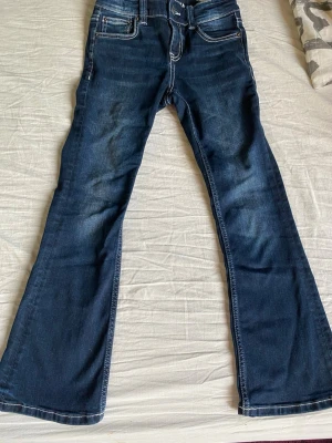 Mörkblå bootcut jeans med kontrastsömmar - Snygga mörkblå bootcut jeans med vita kontrastsömmar och klassisk femficksdesign. Jeansen har normal midja och lätt utsvängda ben. Perfekta för dig som gillar en retroinspirerad look och vill ha ett par jeans som sticker ut lite extra.