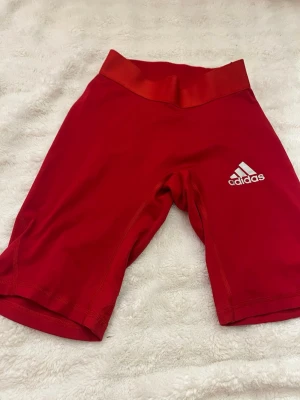 Röda Techfit cykelshorts från Adidas - Säljer ett par röda cykelshorts från Adidas Techfit med ClimaCool-material. De har kompression, elastisk midja och Adidas-logga på benet. Perfekta för träning eller cykling, sitter tight och andas bra.