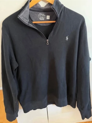 Svart halvzip från Polo Ralph Lauren - Svart långärmad tröja från Polo Ralph Lauren med halv dragkedja och broderad logga på bröstet. Tröjan har en klassisk passform och ribbade muddar vid ärmslut och nederkant. Perfekt för en stilren och avslappnad look. Säljer då den är för kort för mig, använd 2-3 gånger, skriv för pris/frågor!😊
