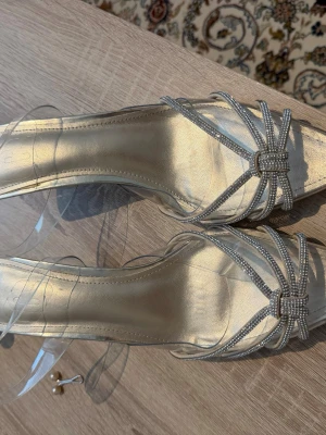 Guldiga pumps med strass och transparenta band - Snygga pumps i guldig nyans med fyrkantig tå, dekorerade med glittrande strassdetaljer och transparenta remmar. Skorna har en elegant design som sticker ut och passar perfekt till en trendig look. Från SHEIN 