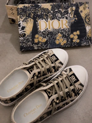 Dior sneakers med monogrammönster - Snygga Dior sneakers i beige och svart med klassiskt monogrammönster och vita sulor. Skorna har låga skaft, beige snörning och detaljerad sula med svart stjärna undertill. Tillverkade i textil med exklusiv känsla och Dior-logga på plösen.