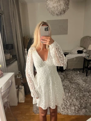Vit spetsklänning med v-ringning - Säljer en kort vit klänning med v-ringning och långa spetsärmar. Från Gina Tricot, använd fåtal timmar på min student.