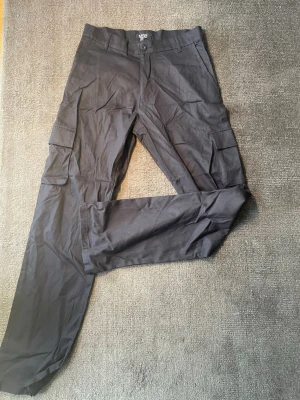 Cargo Chinos - Säljer ett par snygga ”tall relaxed fit” svarta cargo chinos med flera praktiska fickor. Bekväm passform och en minimalistisk design som passar perfekt till både vardag och finare tillfällen.  • Färg: Svart • Modell: Cargo Byxor • Skick: Nyskick, inga defekter. • Rymliga cargofickor på sidorna samt sidofickor framtill.  📦 Skickas snabbt och väl paketerat, samt tvättad och strykt. Hör gärna av dig om du vill ha fler bilder eller mått!