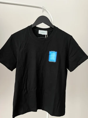 Svart t-shirt från Casablanca - Snygg svart t-shirt från Casablanca med blå grafiskt tryck och texten 'Casa Blanca' på bröstet och ryggen. Klassisk rund hals och korta ärmar. Perfekt för dig som gillar stilrena plagg med en twist. Prislappen finns på fortfarande säljer på grund av att den är lite på mig, priset går att diskutera vid snabb affär