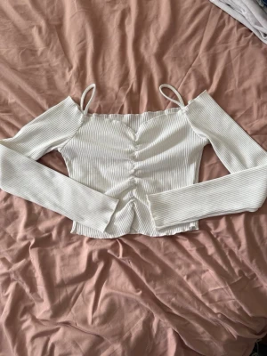 Vit ribbad topp från Dazy (Shein) - Säljer en vit ribbad topp från Dazy med långa ärmar och smala axelband. Toppen har en croppad passform och snygg framtill som ger en cool detalj. Perfekt att styla med jeans eller kjol för en trendig look.