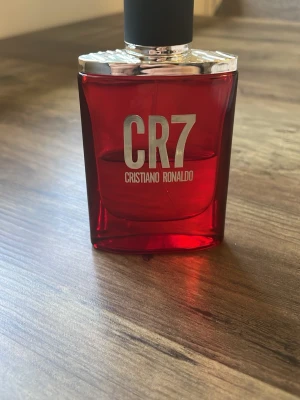 CR7 parfym röd flaska - Snygg parfymflaska i rött glas med silverfärgat lock och tydlig CR7-logga på framsidan. Doften är från Cristiano Ronaldo och flaskan har en modern, stilren design som sticker ut på hyllan.