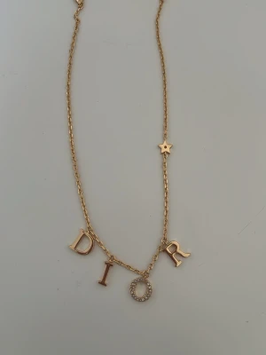 Guldhalsband med bokstäver och stjärna - Snyggt halsband i guldton med hängande bokstäver. O:et är dekorerat med små glittrande pärlor och kedjan har en liten stjärndetalj. Perfekt för dig som gillar statement-smycken och trendiga accessoarer.