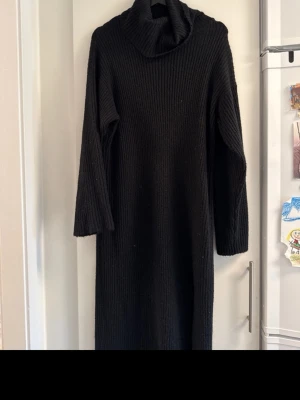 Svart ribbad stickad långklänning med polo - Använd fåtal gånger, i fint skick. Mysig svart stickad långklänning med polokrage och ribbad struktur. Klänningen har långa ärmar och en relaxed passform, perfekt för kyligare dagar. 