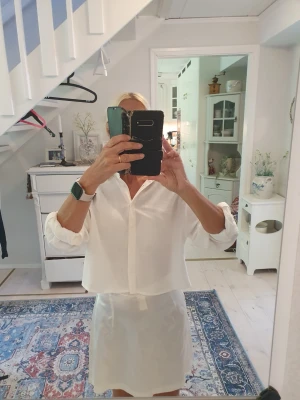 Vit croppad skjorta med knappar - Säljer en stilren vit skjorta med croppad passform och klassisk krage, linneliknande tyg.. Skjortan har långa ärmar och knäppning framtill. Perfekt till jeans eller kjol för en clean look.