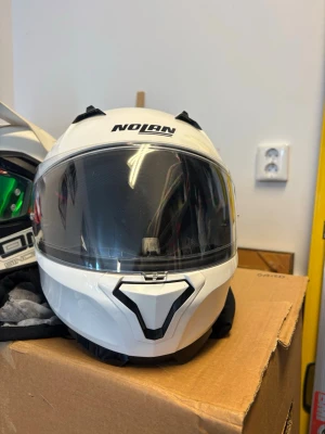 Vit Nolan MC-hjälm med visir - Säljer en vit Nolan motorcykelhjälm med stort klart visir och modern design. Hjälmen har svarta detaljer och ventilation upptill. Perfekt för dig som vill ha både säkerhet och stil på vägen.