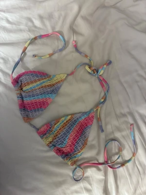 Randig bikiniöverdel i pastellfärger - Säljer en superfin bikiniöverdel med smock och färgglada ränder i pastell. Triangelformade kupor och tunna knytband i matchande färger. Perfekt för stranden eller poolen! Använd en gång. 