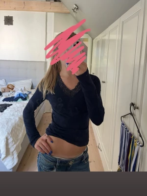 Mörkblå långärmad topp med spets - Säljer en mörkblå långärmad topp med v-ringning och fina spetsdetaljer vid halsen. Toppen har en slim passform och är perfekt att styla med jeans eller kjol. Superenkel men ändå snygg detalj med spetsen vid urringningen.  🩷