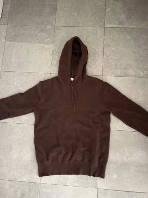 Mörkbrun hoodie med huva - En enkel och stilren mörkbrun hoodie med huva och dragsko. Hoodien har långa ärmar och ribbade muddar vid ärmslut och nederkant. Perfekt för dig som gillar en clean och avslappnad look. Materialet ser ut att vara mjukt och bekvämt. Tröjan är i bra skicka endast ett hål vid armbåge där av de låga priset! Vid frågor eller funderingar är de bara att höra av sig