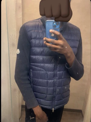 Mörkblå quiltad dunväst Moncler - Snygg mörkblå dunväst från Moncler med quiltad front och ärmar i stickad kvalitet. Västen har dragkedja framtill och Moncler-logga på ärmen. Perfekt för lager-på-lager och en stilren look.