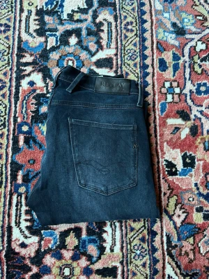 Replay anbass  - Snygga mörkblå/svartaktiga jeans från Replay, modell Anbass. Klassisk slim fit med avsmalnande ben och normal midja. Väldigt clean modell som funkar både till sneakers och lite mer uppklätt.  📏 Storlek: W30 / L32 📐 Jag är: 175 cm / ca 70 kg 👖 Modell: Replay Anbass 🎨 Färg: Mörkblå/svart denim ✨ Passform: Slim fit / tapered 🔄 Stretch i materialet för en skönare passform  Jeansen är i fint begagnat skick och har en snygg, lätt använd denim-look. 