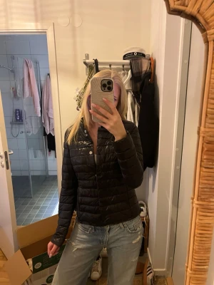 Svart pufferjacka från Amisu - Snygg svart pufferjacka från Amisu i storlek 36. Jackan har quiltad design, hög krage och stängs med knappar framtill. Perfekt för kalla dagar och ger en stilren look till din outfit.
